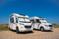 Two Motorhomes parked next to each other on a sunny day.