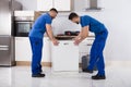 Two Movers Placing Dishwasher In Kitchen Royalty Free Stock Photo