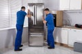 Two Movers Placing Refrigerator In Kitchen