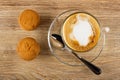 Two muffins, spoon, cappuccino in glass cup in saucer on wooden table. Top view Royalty Free Stock Photo