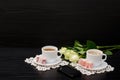 Two mugs of coffee with milk, smartphone, Turkish delight on a saucer, white roses on a black background. Royalty Free Stock Photo