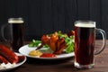 Two mugs of dark beer with crusty grilled chicken wings and vari Royalty Free Stock Photo