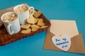 Two mugs of hot coffee with marshmallows on a wicker tray, heart-shaped cookies, an envelope and a blank sheet of paper. Royalty Free Stock Photo