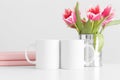 Two mugs mockup with pink tulips in a pot and books on a white table