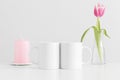 Two mugs mockup with pink tulips in a vase and candle on a white table
