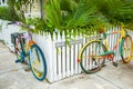 Two multi-colored cycles attached to white picket fence as street art