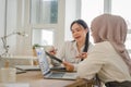 Two multi ethnic female office workers discussing financial market data and comparisons in the office.