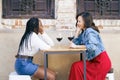 Two multiethnic friends talking sitting at a table outside a bar while drinking a glass of red wine. Royalty Free Stock Photo