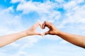 Two multiethnic hands join together to form a shape heart with a blue sky clouds background. Concept of hope