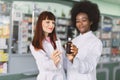 Two multiethnic pharmacists women, African and Caucasian, working in drugstore, checking medicines quality at hospital