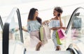 Two multiethnic women on escalator in shopping mall Royalty Free Stock Photo