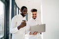 Two multiracial cheerful corporate employees are talking while standing with laptop in the middle of the office. Royalty Free Stock Photo