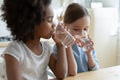 Two multiracial girls sit in kitchen feels thirsty drink water