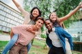 Two multiracial teenage student best friends giving a piggyback ride to their girlfriends. Young men smiling and having Royalty Free Stock Photo