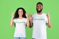 Two Multiracial Volunteers Pointing Fingers Up Standing Over Green Background