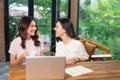 Two multiracial young female friends surfing the internet together on a laptop as they sit in a cafeteria enjoying a cup of coffee Royalty Free Stock Photo