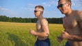 Two muscular men running outdoors. Young athletic guys jogging over the field. Male sportsmans training together at