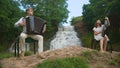 Two musicians Accordionist and bandurist playing on the rocks at waterfall