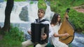 Two musicians Pianist and bandurist playing on the rocks at waterfall