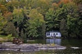 Two Muskoka chairs sitting on a rocky shore facing a calm lake with trees and a white cottage in the background Royalty Free Stock Photo