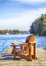 Two Muskoka chairs on a wood dock at a blue lake Royalty Free Stock Photo