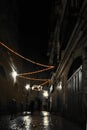 Two mysterious silhouettes of people on a dark street with a Christmas garland. Dark nightly narrow streets of the old city,