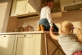 Two naughty kids, brother and sister trying to find something sweet in the kitchen cupboard. Little girl helping her