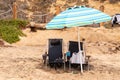 Two navy blue rusty beach chairs under a light blue striped umbrella on a beach. Royalty Free Stock Photo