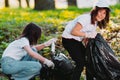 Two nice girls spending their time in voluntary mission outdoors in gathering garbage in the park and putting it into Royalty Free Stock Photo