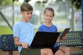Two nice kids, teenager boy holding laptop computer and pretty young girl with digital tablet looking at screen outdoor