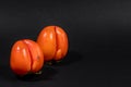 Two non-standard ugly ripe orange persimmons on black background with copy space for text.