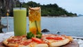 Two nonalcoholic cocktails glasses with straws, fresh pizza on beach cafe table. Tropical resort vacation calm sea bay Royalty Free Stock Photo