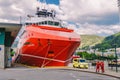 Two Norwegian paramedics in red uniforms are resting near an ambulance parked in a port near a large ship. Theme healthcare and