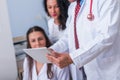 Two nurses female physicians and a male doctor looking in a tablet at the doctor`s office while discussing a medical report