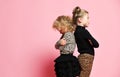 Two offended kid girls friends sisters in leopard print clothes are standing with their backs to each other on pink