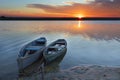 Two old blue-green boats stand on the bank of a calm river against the background of a bright rising sun Royalty Free Stock Photo