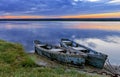 Two old dilapidated boats are moored with a metal chain to the bank of a calm river in the early morning against the backdrop of a Royalty Free Stock Photo