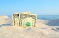 Two old dollar bills in sand on background of sea blue sky on sunny summer Royalty Free Stock Photo