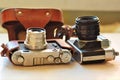 Two old school vintage photo cameras on light brown table. One in brown retro leather case holder