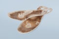 Two old, shabby orthopedic insoles isolated on blue background. Dirty leather insoles. Worn out things with holes. Inner