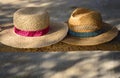 Two old straw hats, one for a woman and one for a man, lie side by side on a wooden bench in the shade, with space for text Royalty Free Stock Photo