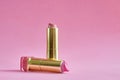 Two old used lipstick tubes on pink background