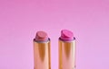 Two old used lipstick tubes stand on a pink background