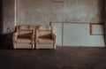 Two old white upholstered armchairs and white planks in front of cement wall