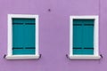 Two old windows with light blue shutters on light violet wall Royalty Free Stock Photo