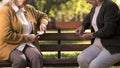Two old women enjoying cards playing on bench in park, elderly friends leisure