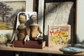 Two old wooden dolls with broken hands are placed on an old book lying on the counter. World map, board game and watercolor