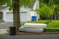 Two old worn out mattresses by a tree at the curb near a trash can in front of a house