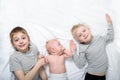 Two older brothers are lying with the youngest baby in a white bed. Happy childhood, big family Royalty Free Stock Photo