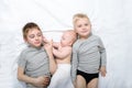 Two older brothers play and laugh with the youngest baby in a white bed. Happy childhood, big family Royalty Free Stock Photo